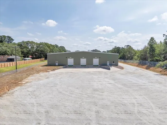 Front view of the C5 Warehousing facility from a distance, showing three loading dock doors, a wide gravel lot for truck access, and a secure fenced perimeter surrounded by trees.