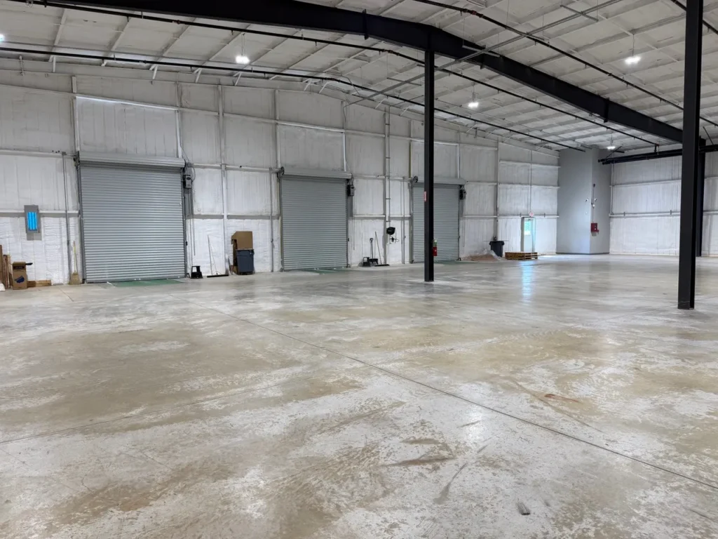 docks-inside-image Spacious interior of the C5 Warehousing facility featuring polished concrete floors, high ceilings with industrial lighting, and three large roll-up loading dock doors for logistics operations.