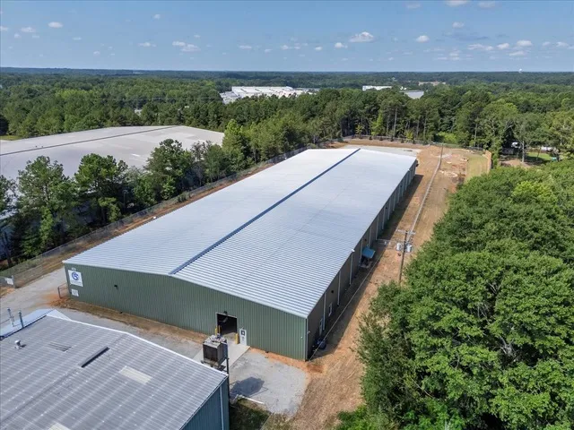 Aerial view of the C5 Warehousing facility showing a long warehouse building with a metal roof, secure fencing, and surrounding trees in an industrial area.