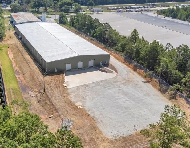 Aerial view of the C5 Warehousing facility showing a large warehouse building with multiple loading docks, a secured fenced perimeter, and a spacious paved lot surrounded by trees.
